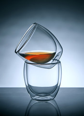 Two glasses for coffee or tea, standing on top of each other with tea in the upper glass with reflection