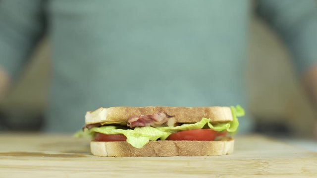 Tasty BLT sandwich with red tomatoes, lettuce, bacon on a wooden board. Man or cook press it with hands.