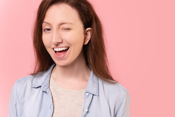 Close-up portrait of a cute and cheerful caucasian young woman having a fun winking eye posing over...