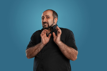 Close-up portrait of a brunet middle-aged man with beard, dressed in a black t-shirt and posing against a blue background.