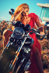 Fototapeta na wymiar Gorgeous woman wearing red fluffy dress sitting on motorcycle posing outdoors