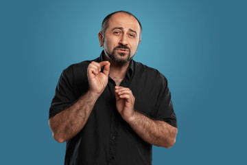 Close-up portrait of a brunet middle-aged man with beard, dressed in a black t-shirt and posing against a blue background.