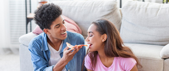 Playful black girl tasting her boyfriend's pizza