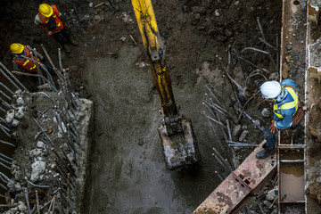 asian construction workers laborers and excavator backhoe working for footing foundation on site of new route sky train construction in Bangkok, Thailand.