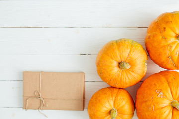 Orange pumpkins with gift in brown paper package tied up with strings on old white wooden background Thanksgiving and Halloween concept. Top view. Copy space for text and design