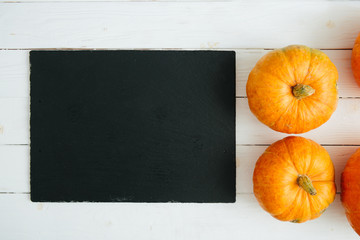 Pumpkins on wite wooden background and black slate stone surface. Thanksgiving and Halloween...