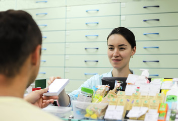 Woman pharmacist standing at the cash register sells medicine to a man