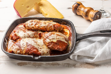 Parmegiana Steak also known as Filet Parmegiana in a black iron pan on a wooden white background, cheese and tomato sauce. Soft light, angle view