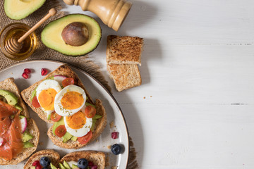 Avocado toast with different topping including salmon fish, eggs, berries, healthy and organic food, breakfast meal on white wooden background