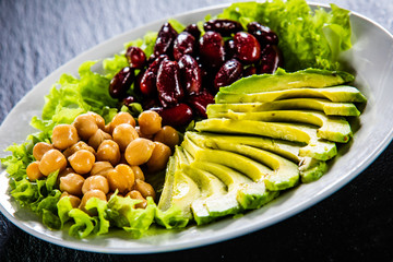 Vegetable salad with chickpea, avocado and red beans in bowl on black stone 