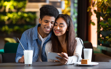 Couple of teenagers watching photos on phone in cafe