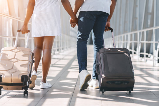 Black millennial couple walking with luggage at airport