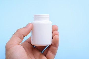 Hand holding white plastic bottle over the blue medicine background