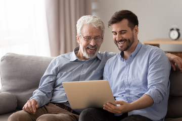 Senior father and adult son using laptop looking at screen