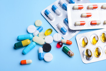 Pills, capsules and packed medicine in foil and zip packing on light blue background