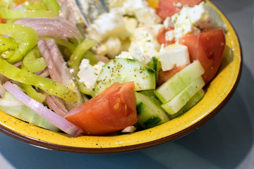 Greek salad with vegetables and feta cheese close up. Vegetable dish of onions, peppers, tomatoes, cucumbers and cheese in a yellow plate.