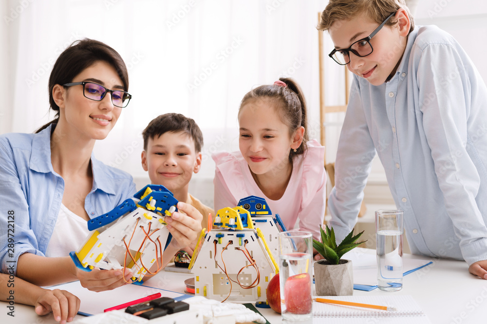 Poster teacher showing modern robot to children in classroom