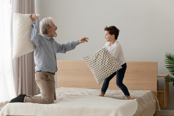 Funny happy grandfather and grandson enjoy pillow fight on bed
