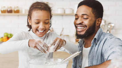 Cute black girl adding eggs into dough bowl