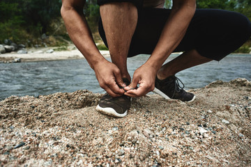 Athlete runner tying shoelaces before a morning jogging on the river, Kazakh jogger in nature close-up
