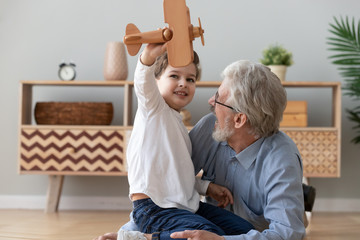 Happy old grandfather and cute grandson playing with wooden plane