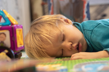 Toddler child kid boy fell asleep on floor in nursery among toys.