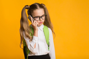 Discontented Elementary Student Girl Holding Cellphone To Ear, Studio Shot