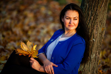 Golden autumn. Beautiful brunette caucasian woman in a blue cardigan in the city park at sunset....