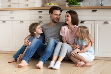 Happy family of four sitting on wooden floor at kitchen.