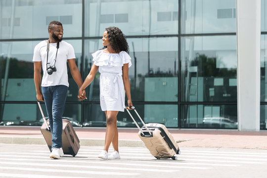 Happy black millennials going out of airport with luggage