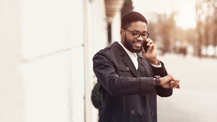 Young businessman talking on cellphone and looking at watch