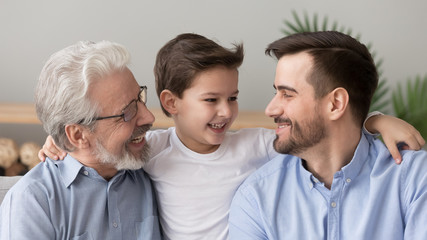 Cute happy boy grandson embracing young father and old grandfather