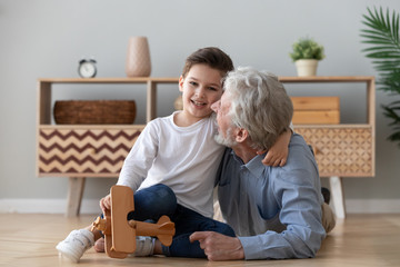 Happy old grandad embracing cute small grandson looking at camera