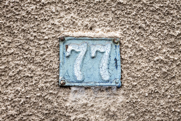 Number 77, seventy-seven, street number sign on the wall	