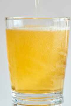 Photograph of a glass tumbler with its reflection in which a cold beer is falling, on a white background.