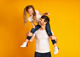 Father Giving His Daughter Piggyback Ride Gesturing Thumbs-Up In Studio