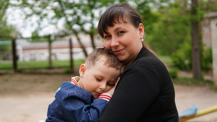 Fototapeta na wymiar Smiling woman hug cute little boy on playground. Boy close eyes