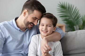 Affectionate dad and child son bonding embracing sit on sofa