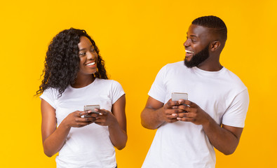 Cheerful black millennial couple browsing on smartphones