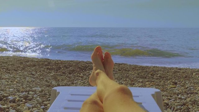 View of the feet from the first person, a man lying on the seashore.
