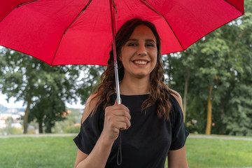 A smiling gothic girl holding red umbrella outdoors