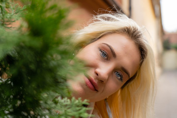 A blonde girl peekы out from behind a green branch