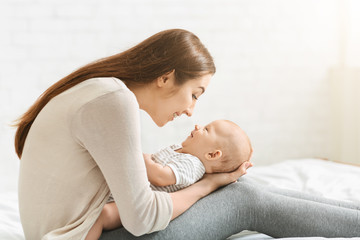 Young mother playing with adorable baby in bed