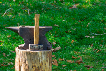 On the stump of a blacksmith's tools: hammer and anvil. The concept of manual labor, craft. Copy space