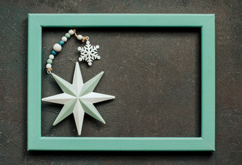  metallic blue star and snowflake in a blue wooden frame on a rough dark textured background. Christmas decor in a frame with a space for text