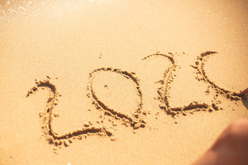 Happy New Year 2020, handwritten on sandy beach. 2020 numbers inscription on golden sand at sea beach. Tropical celebration.