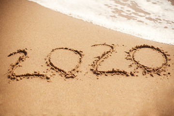 2020 New Year. 2020 written on sandy beach with wave foam at sea beach. Happy New Year. Tropical celebration. Inscription on golden sand.