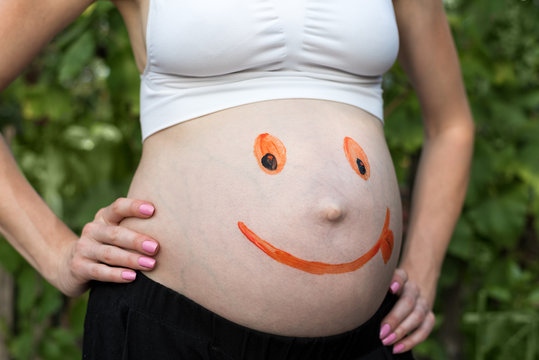 Belly of a pregnant woman with a painted smiling face. Green background