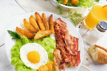 Morning breakfast with delicious fried bacon, French fries and tender egg, close-up.