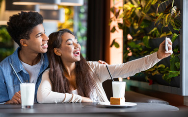 Cheerful mixed race teen couple making selfie at cafe
